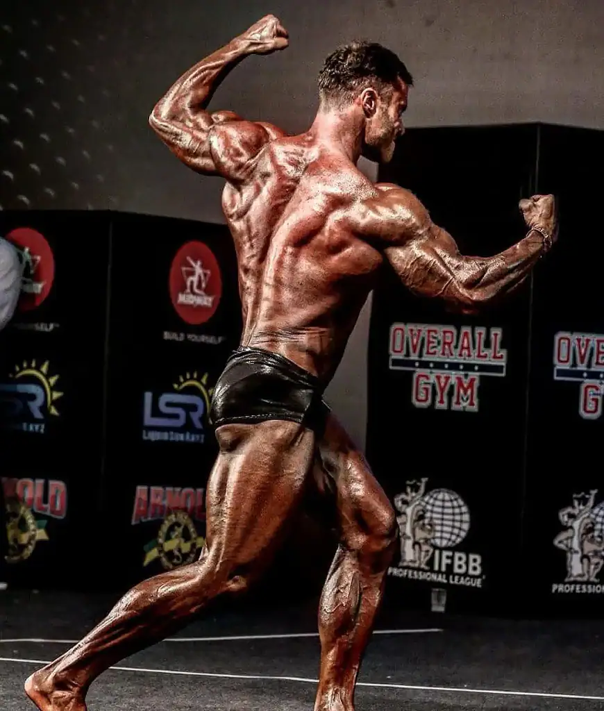 Homem musculoso exibindo definição muscular em evento de fisiculturismo.